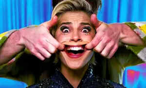 Manos estiran la boca de una mujer para crear una sonrisa forzada. Sus ojos están muy abiertos y maquillados.