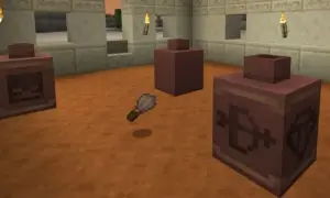 Un pincel de Minecraft flota sobre el suelo de arena, cerca de tres recipientes de arcilla con símbolos grabados.