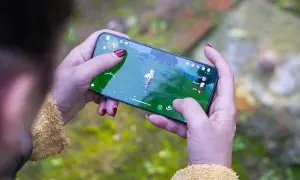 Jugando uno de los mejores juegos móvil, una persona con uñas rojas sostiene un smartphone con un personaje de fantasía en pantalla.