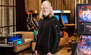 El CEO de Twitch, con su característico cabello rubio, posa sonriente rodeado de máquinas de arcade y un pinball de Stranger Things.