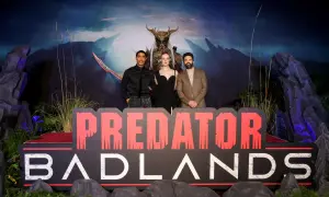 El reparto de Predator: Badlands posa frente a un telón de fondo dramático y un letrero.