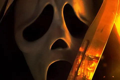 La máscara de Ghostface se acerca, con un cuchillo reflejando un incendio. El terror regresa en Scream 7.