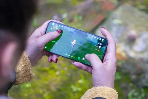 Jugando uno de los mejores juegos móvil, una persona con uñas rojas sostiene un smartphone con un personaje de fantasía en pantalla.