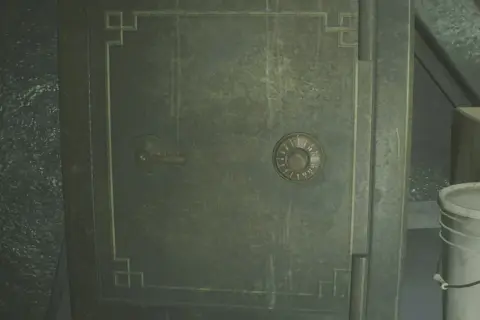 Caja fuerte verde con dial numérico y palanca, junto a un cubo blanco.