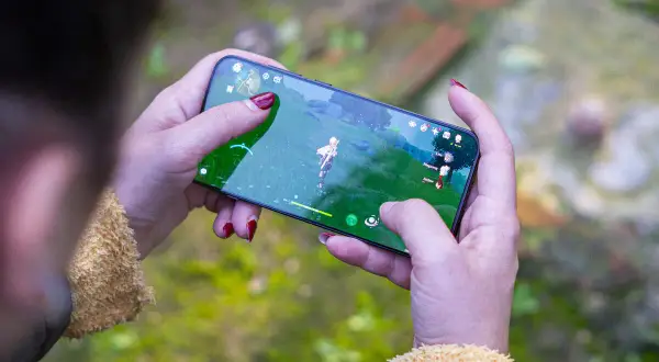 Jugando uno de los mejores juegos móvil, una persona con uñas rojas sostiene un smartphone con un personaje de fantasía en pantalla.