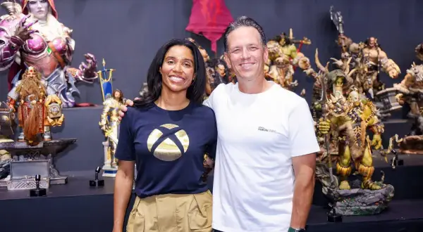 Phil Spencer y una colega posan sonrientes entre figuras de fantasía, incluyendo orcos y elfos.