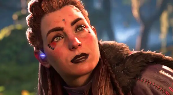 Aloy, la heroína de Horizon, mira al cielo con determinación. Su rostro está adornado con marcas tribales y su cabello recogido en un peinado elaborado.