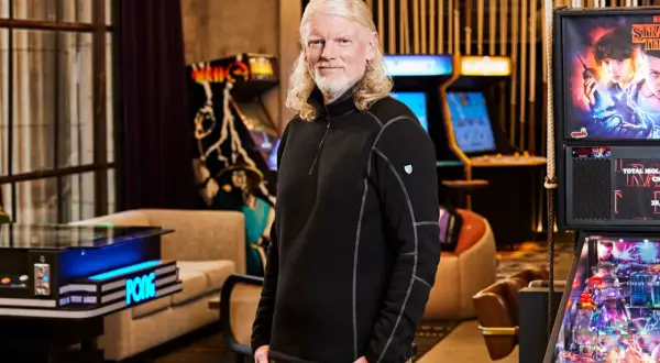 El CEO de Twitch, con su característico cabello rubio, posa sonriente rodeado de máquinas de arcade y un pinball de Stranger Things.