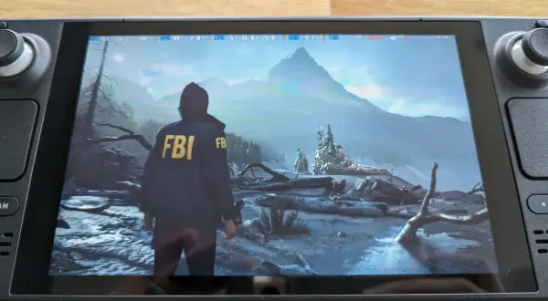 Alan Wake 2 en Steam Deck, con un personaje con chaqueta del FBI en un paisaje nevado y montañoso.