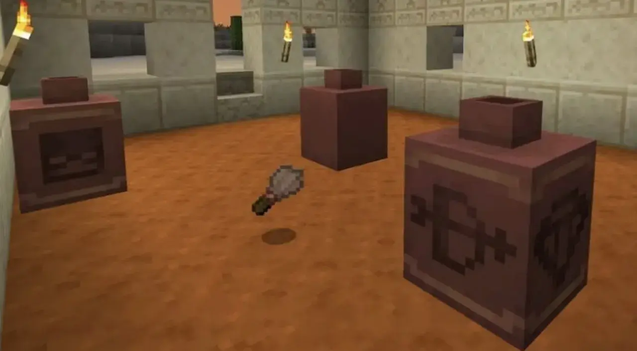 Un pincel de Minecraft flota sobre el suelo de arena, cerca de tres recipientes de arcilla con símbolos grabados.