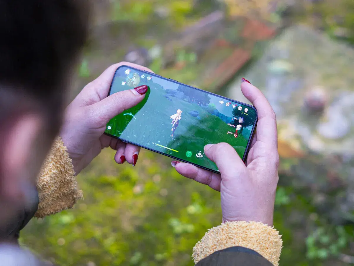 Jugando uno de los mejores juegos móvil, una persona con uñas rojas sostiene un smartphone con un personaje de fantasía en pantalla.