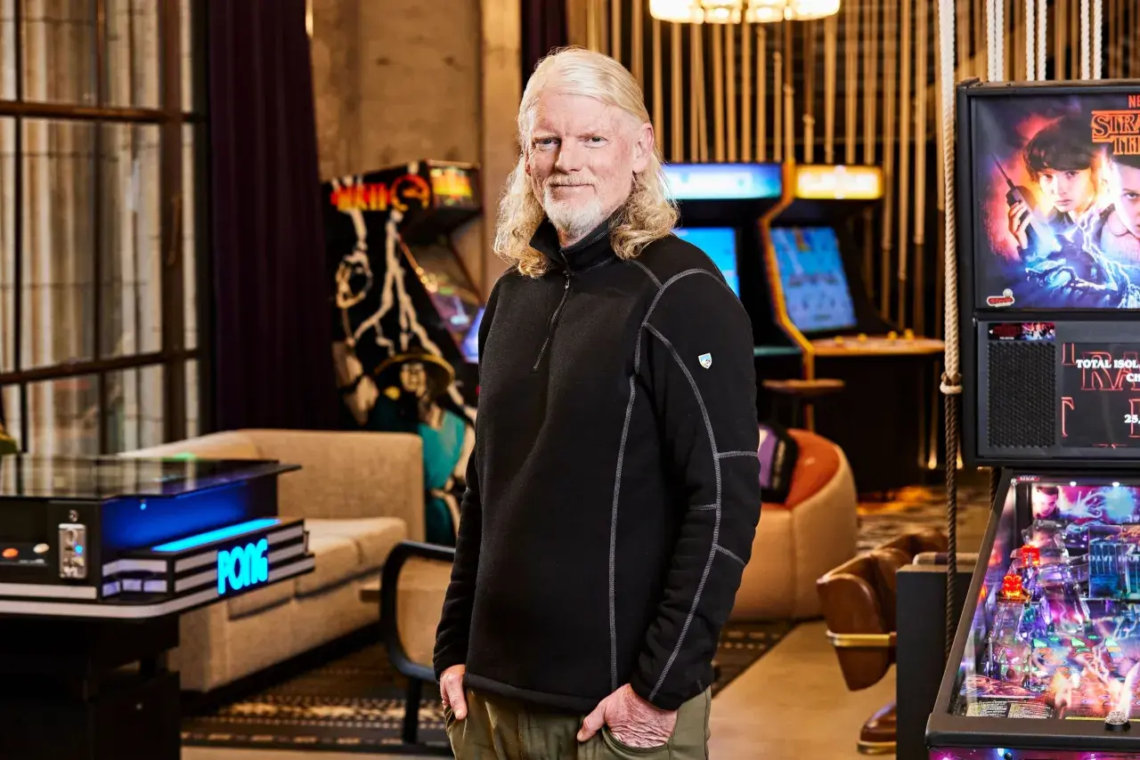 El CEO de Twitch, con su característico cabello rubio, posa sonriente rodeado de máquinas de arcade y un pinball de Stranger Things.