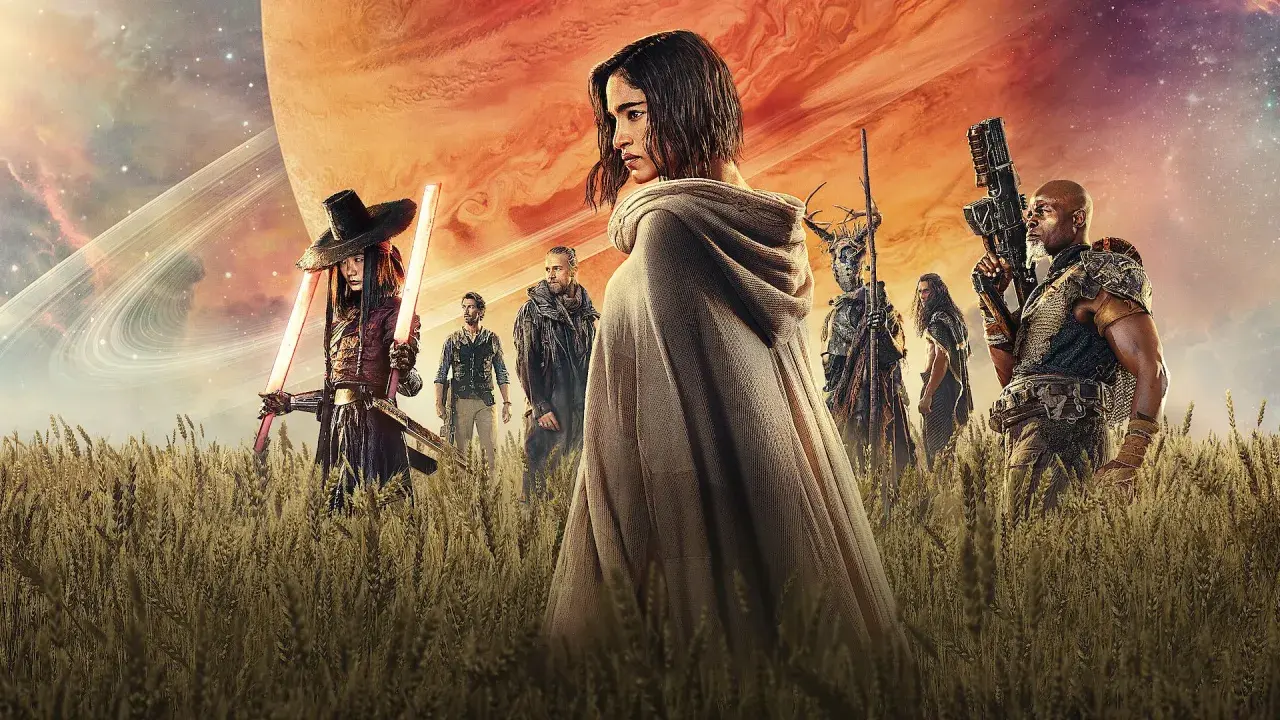 Un grupo de guerreros, incluyendo a una mujer con capa y espadas de luz, se alza en un campo de trigo bajo un cielo anaranjado y un planeta gigante. Son los rebeldes de Rebel Moon.