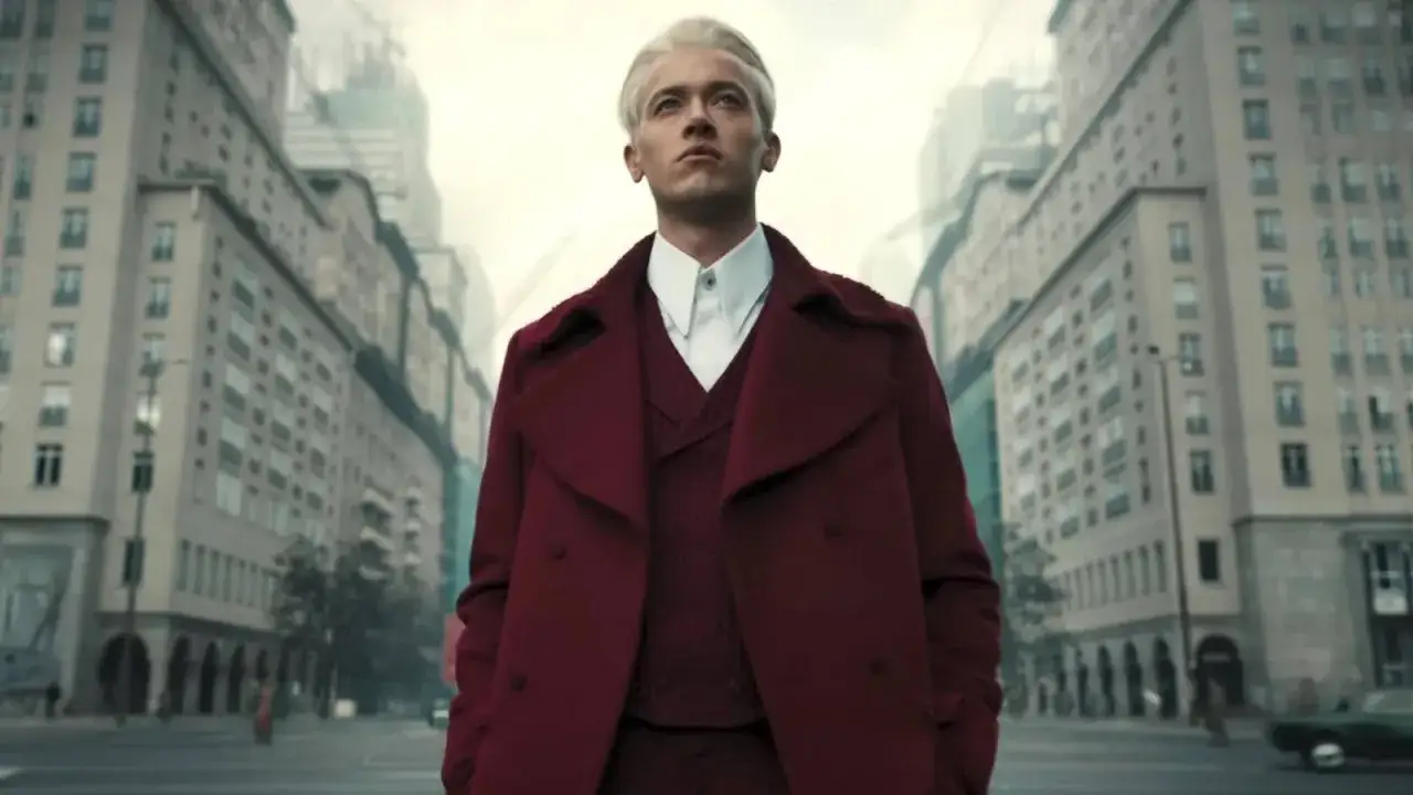 Joven Snow, con su rubio cabello y abrigo granate, camina por una ciudad desolada, anticipando los Juegos del Hambre.