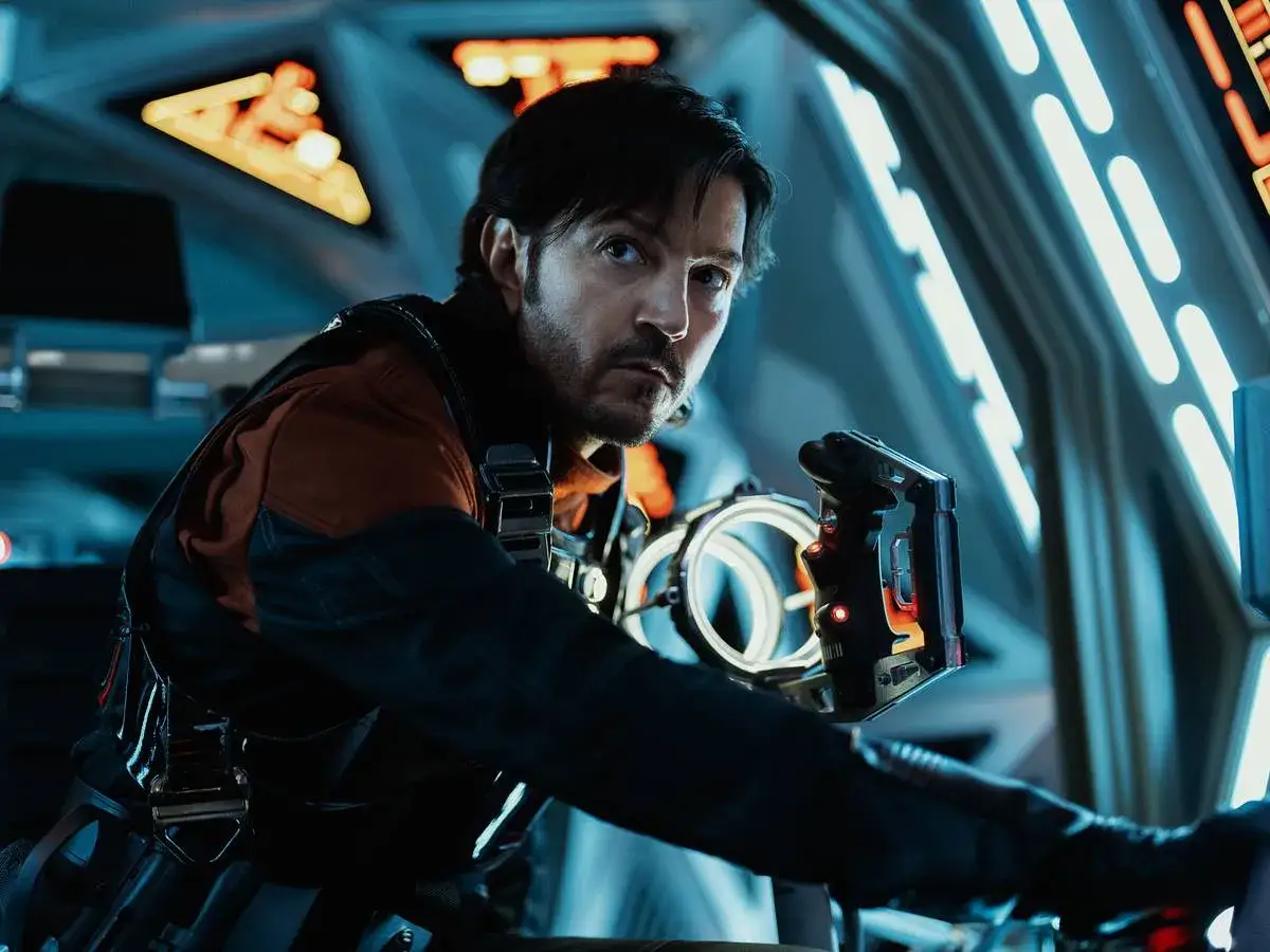 Cassian Andor, con su mirada intensa, se prepara para la acción en la Andor temporada 3. Sostiene un dispositivo futurista en una nave.