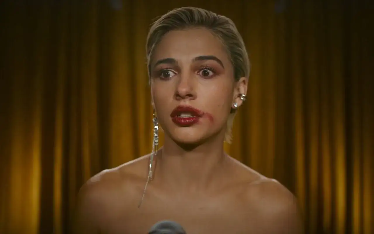 Una mujer con maquillaje corrido y un labial rojo intenso, con una expresi&oacute;n de sorpresa. Su sonrisa parece forzada, casi un rictus.