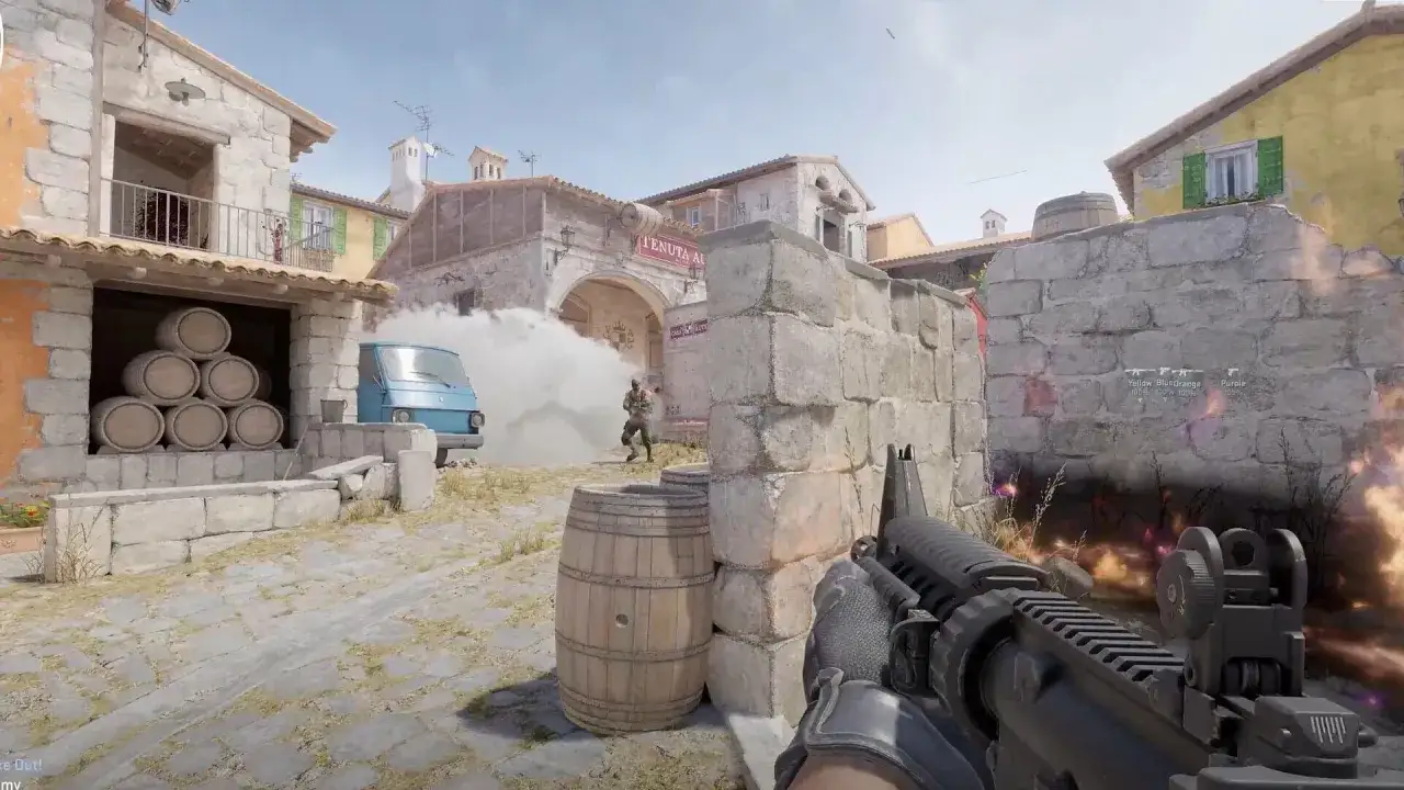 Jugador en Counter-Strike 2 se esconde tras un muro de piedra, con barriles y un veh&iacute;culo azul en un pueblo.