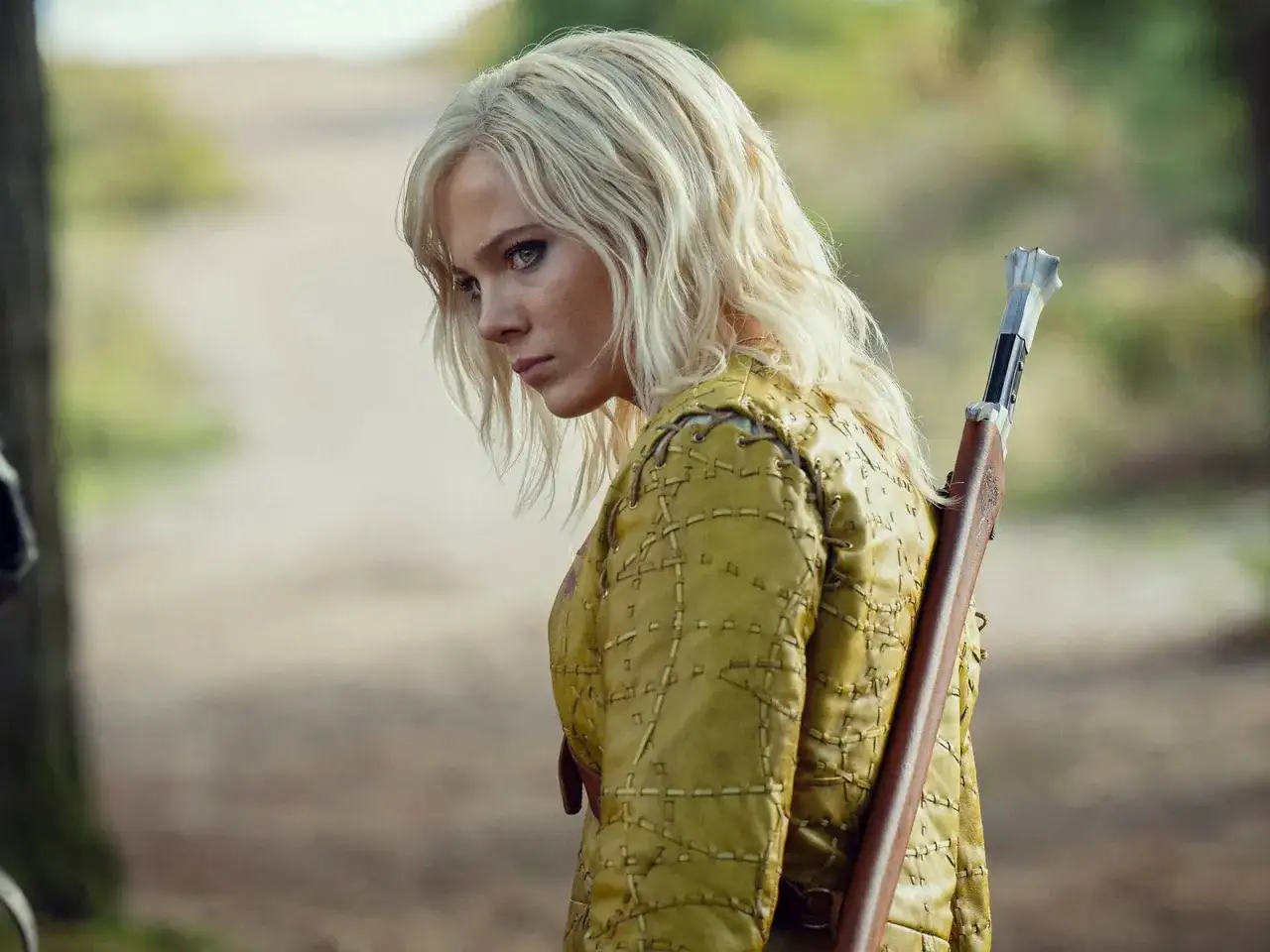 Ciri, con su icónico cabello rubio y mirada intensa, se prepara para la acción en la the witcher temporada 5. Lleva una armadura amarilla y una ballesta a la espalda.