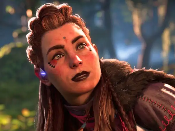 Aloy, la heroína de Horizon, mira al cielo con determinación. Su rostro está adornado con marcas tribales y su cabello recogido en un peinado elaborado.